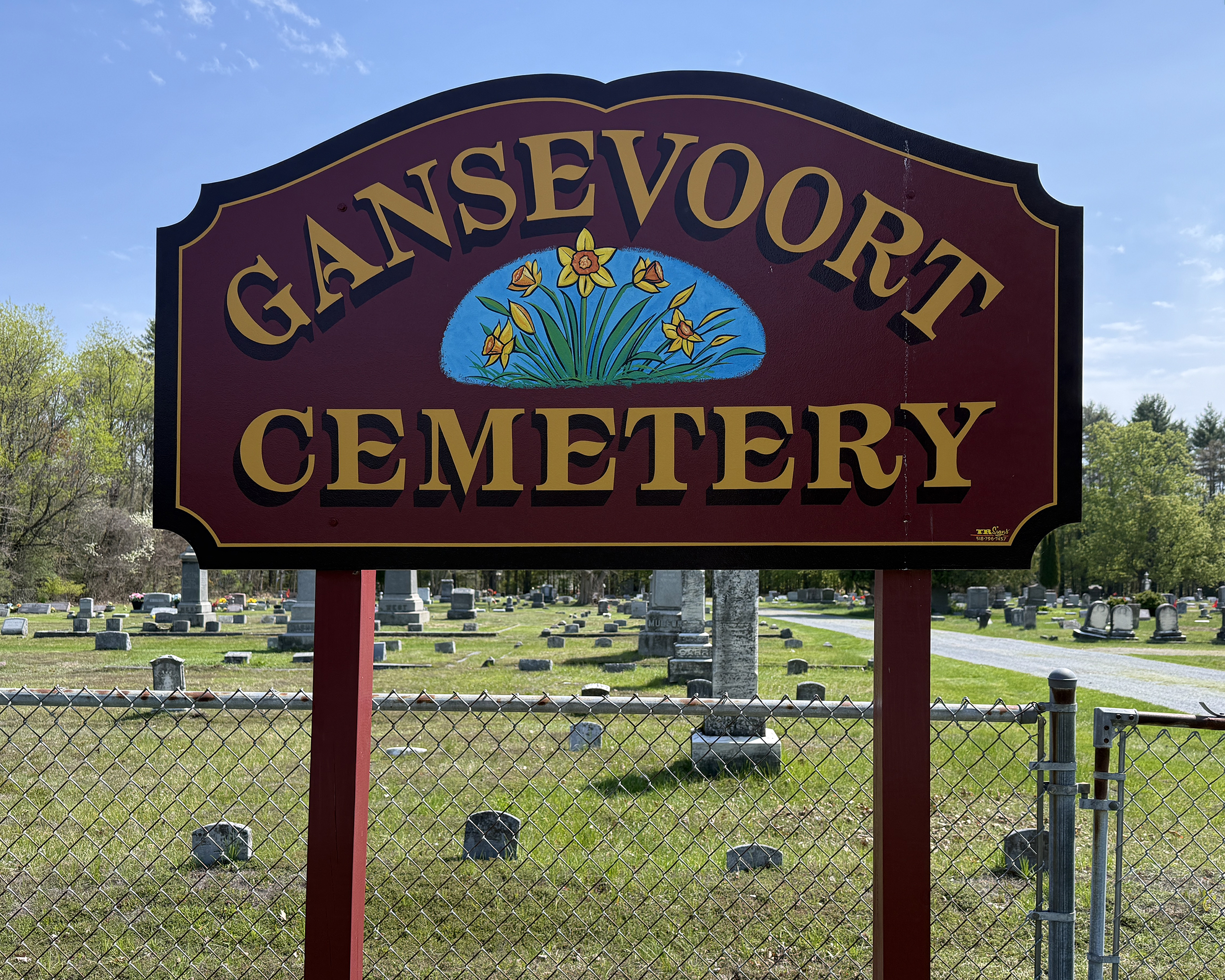 Gansevoort Cemetery Entrance Sign with a chain-linked fence and gravestones in the background in Gansevoort, New York.
