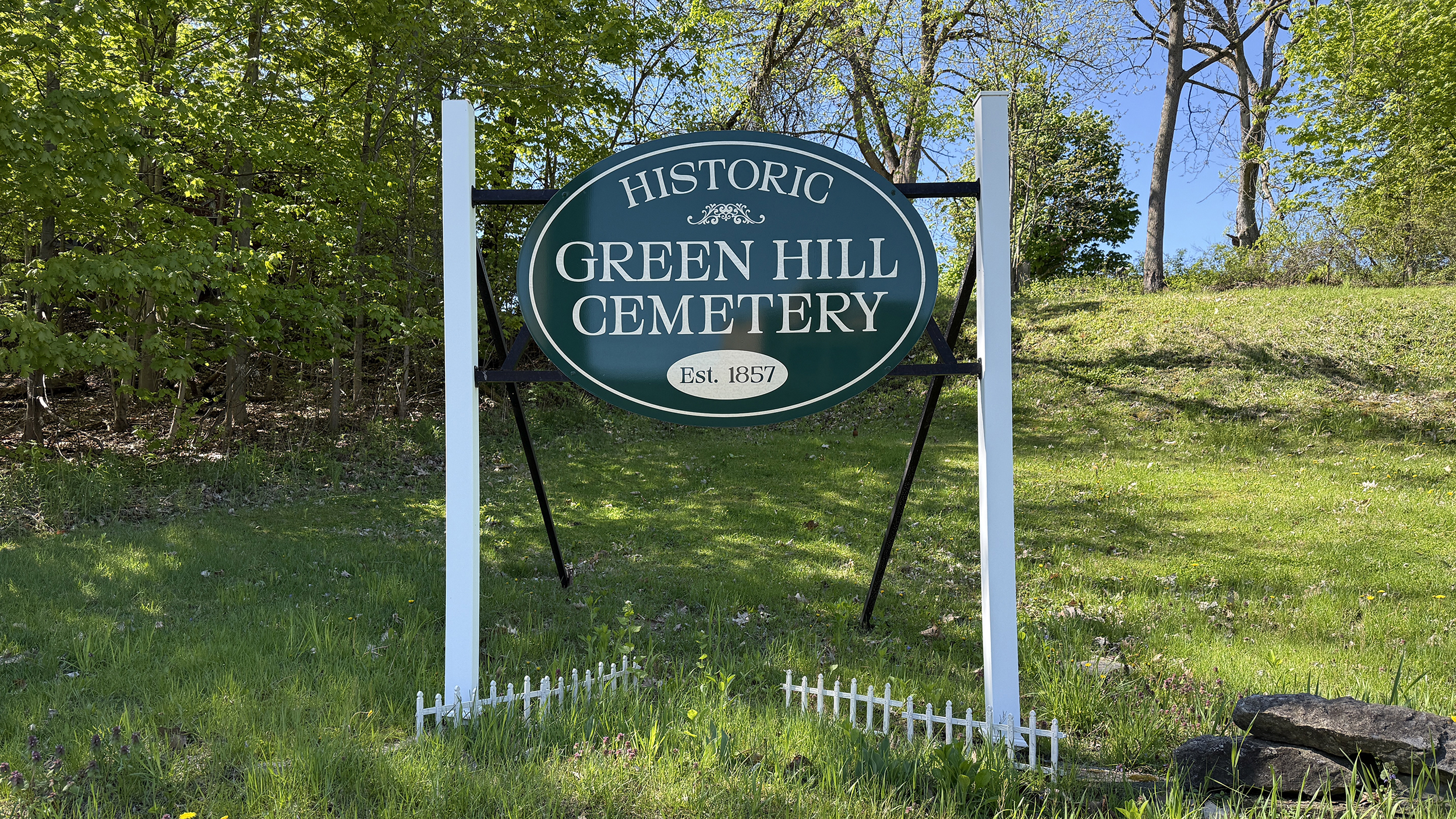 Green Hill Cemetery entrance sign in Amsterdam New York with wooded cemetery hillside behind it