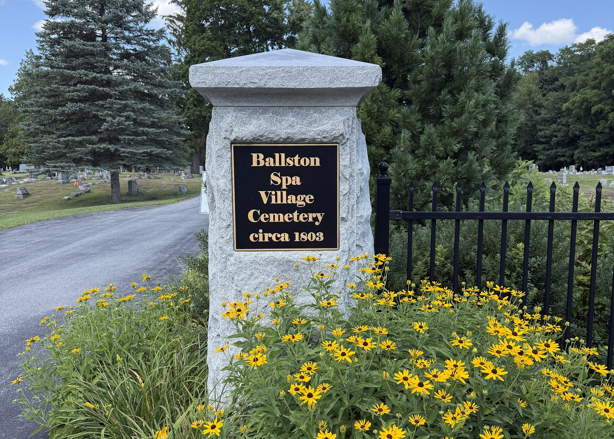 Ballston Spa Village Cemetery entrance sign in Ballston Spa, New York with landscaped flowers and stone marker