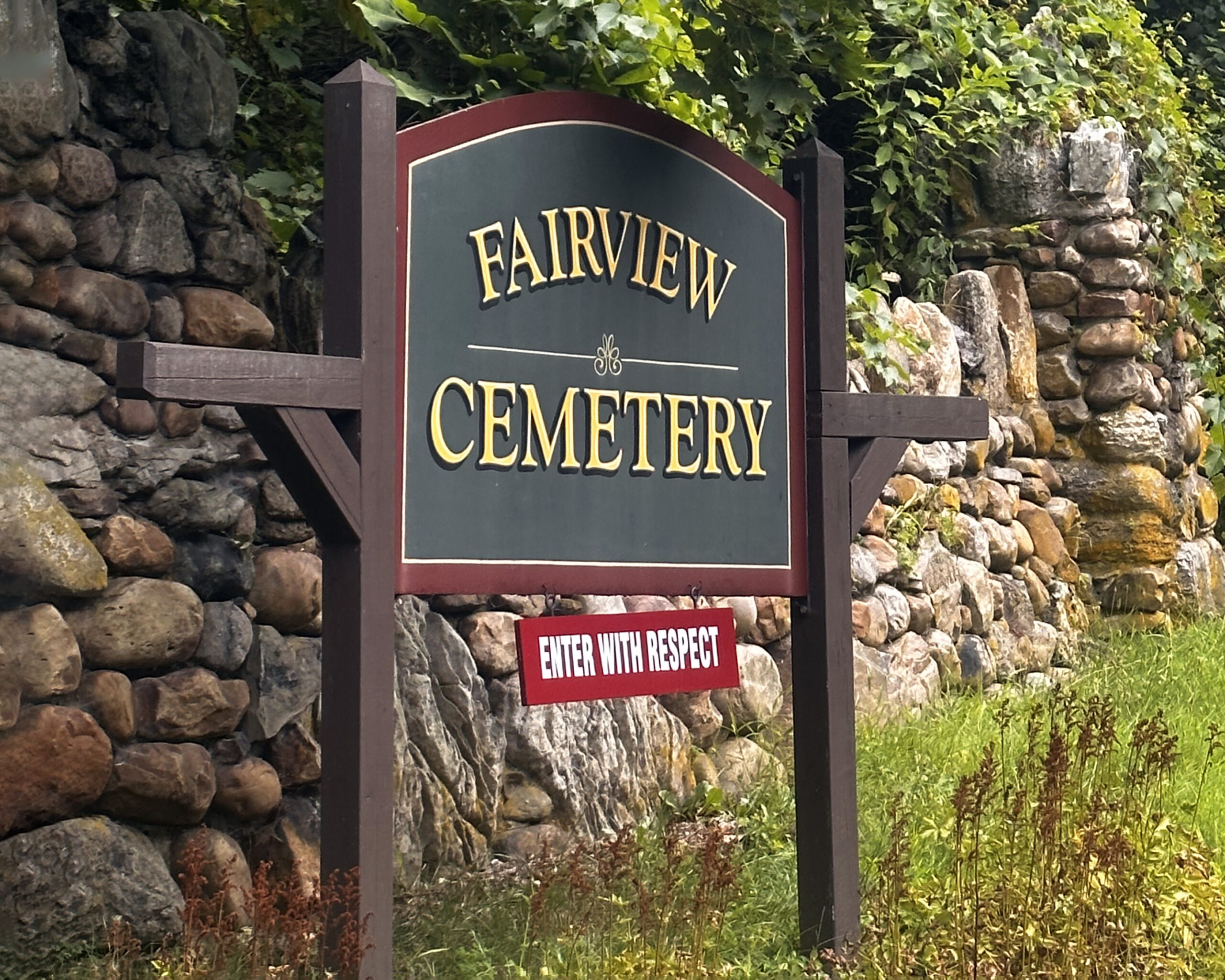 Fairview Cemetery entrance sign in Amsterdam New York with stone wall and wooded cemetery entrance